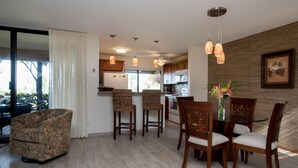 A modern kitchen with a dining area, featuring a glass table, wooden chairs, and pendant lighting. - Ekahi 29C, Ocean View,  Steps away from the pool (Wailea)