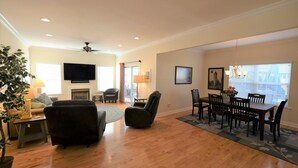A spacious living room with hardwood flooring, a fireplace, a dining area with a table and chairs, a television mounted on the wall, and a ceiling fan. - Less than 2 miles to the beach and boardwalk! (Rehoboth Beach)