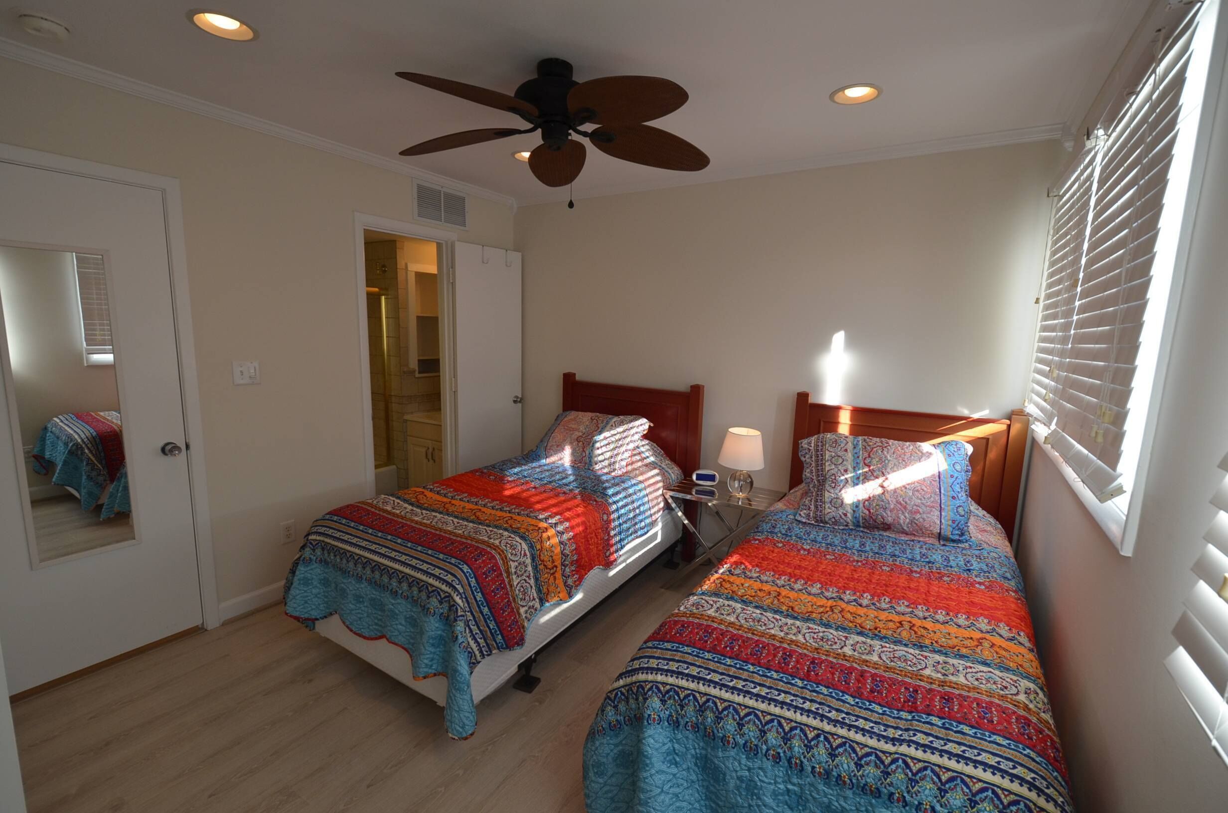 A bedroom with two beds, a ceiling fan, and a window with blinds.
