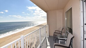 A balcony with a view of the beach and ocean. There are two chairs and a table on the balcony.