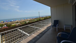 Un balcón con vista a la playa, que incluye barandilla, una silla y una mesita.