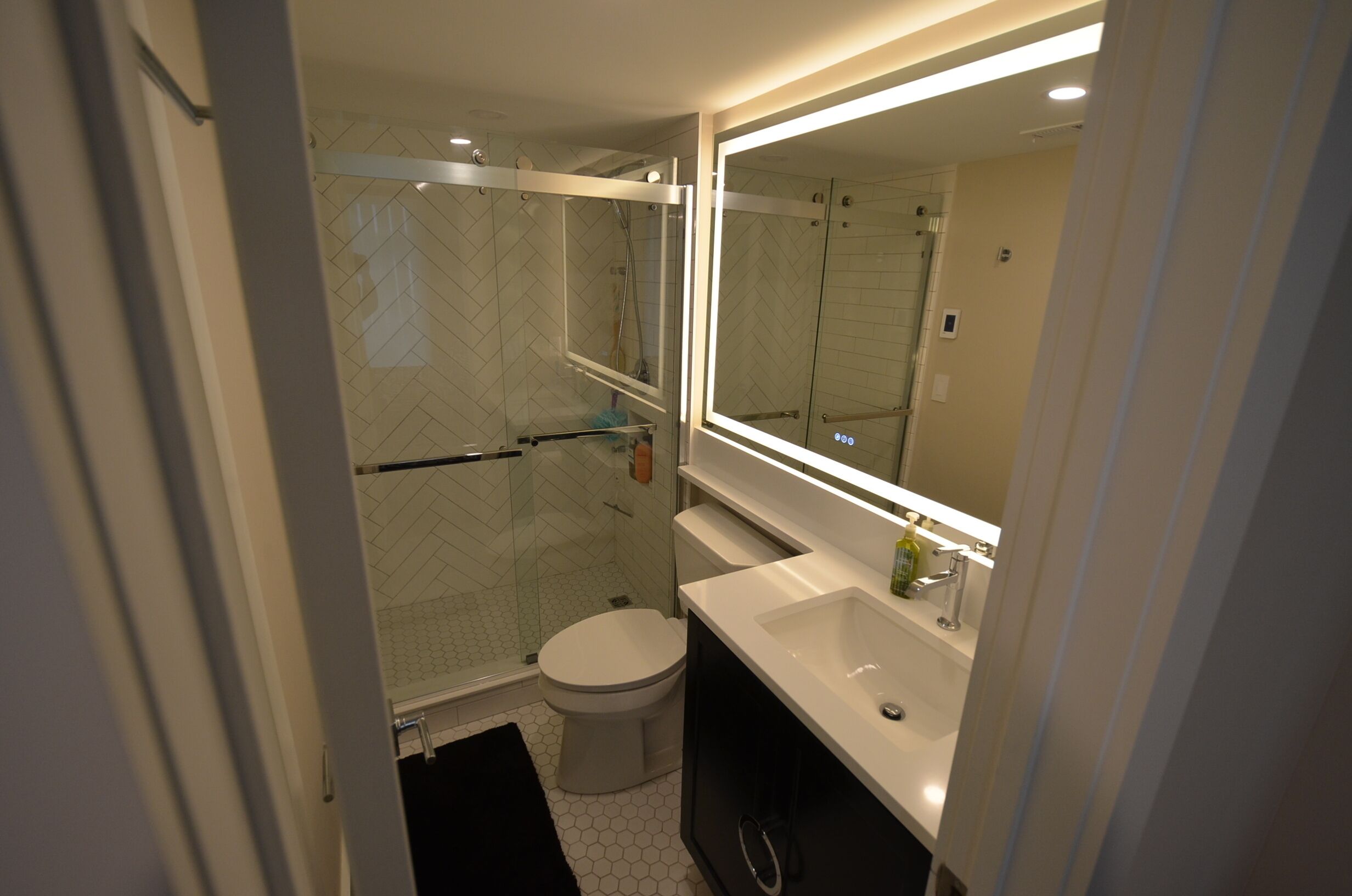 A modern bathroom with a glass-enclosed shower, a white toilet, and a vanity with a mirror.