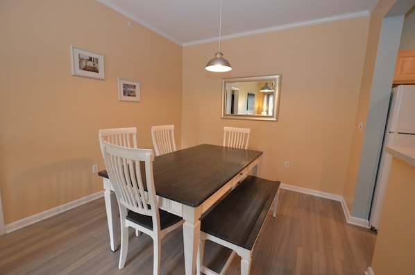 Un coin repas avec une table en bois foncé, des chaises blanches et un luminaire suspendu.