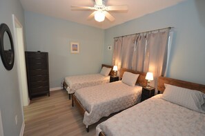 Une chambre avec deux lits, une commode, un ventilateur de plafond et un rideau de douche.