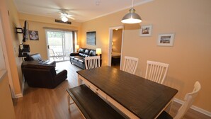 A dining area with a wooden table, white chairs, and a bench. There is a sofa and a television in the background. - ENJOY the Community Pool & Tennis Court! (Rehoboth Beach)