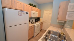 A compact kitchen with wooden cabinets, a white refrigerator, a microwave, and a stove. - ENJOY the Community Pool & Tennis Court! (Rehoboth Beach)