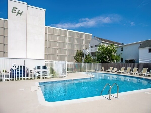 Una piscina con cerca blanca, sillas de descanso y un edificio con la leyenda 'EH'.