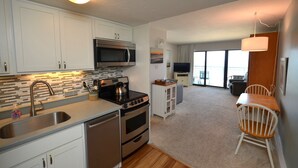 A modern kitchen with stainless steel appliances, a large window, and a dining area with a wooden table and white chairs. - Edgewater House - Ocean Front Units With Spectacular Views! (Rehoboth Beach)