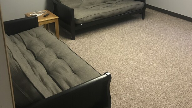 Une pièce avec un canapé gris et un fauteuil plus petit, un tableau encadré au mur et deux enseignes lumineuses sur les murs.