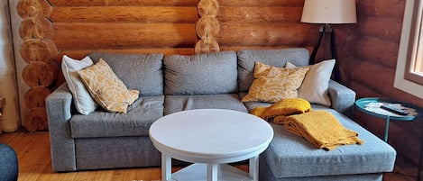 Een gezellige woonkamer met een grijze bank, een ronde witte tafel en een lamp.