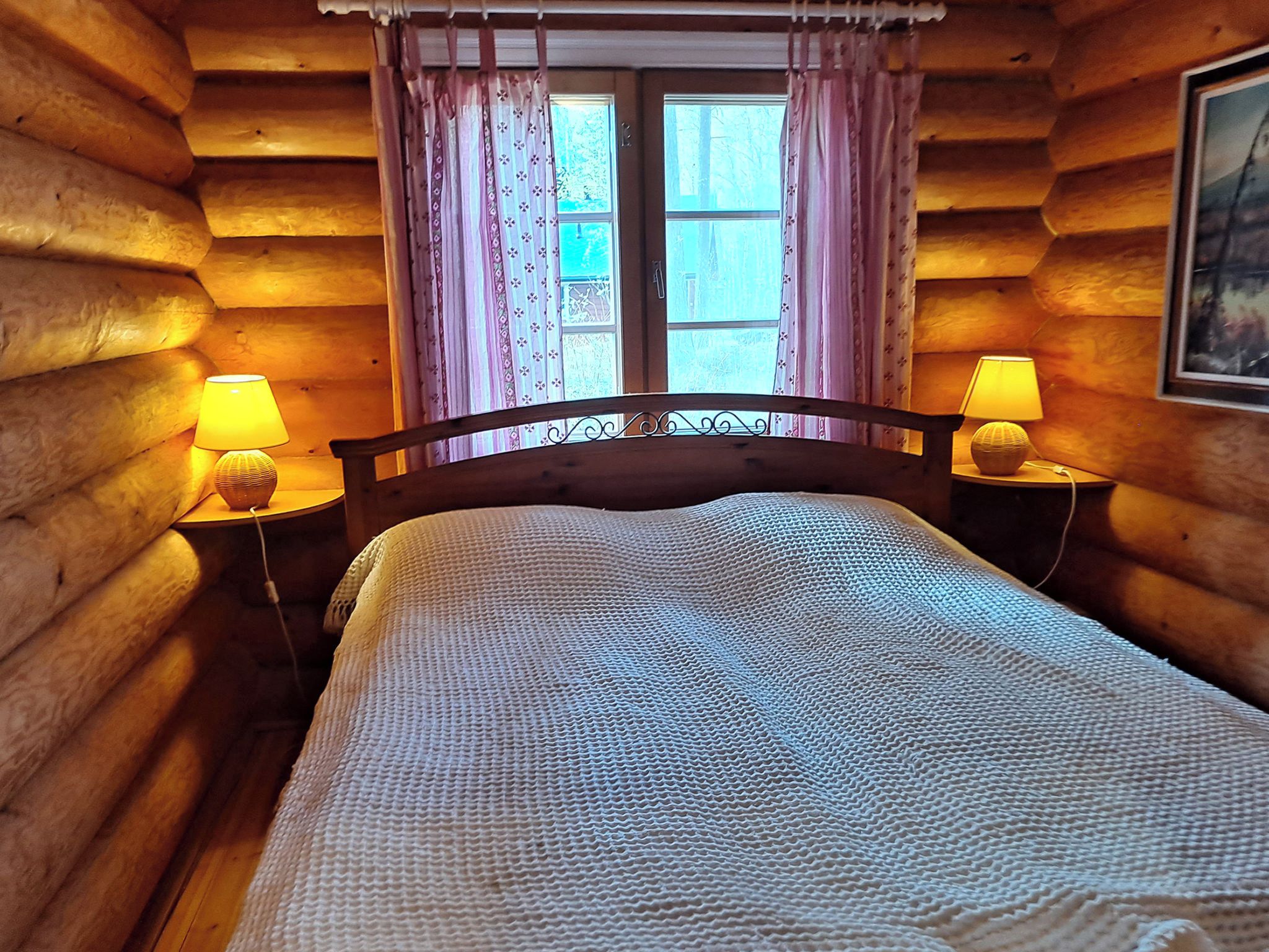 Une chambre dans un chalet en bois, avec un lit, deux lampes de chevet et une fenêtre avec des rideaux.
