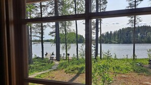 Une vue à travers une fenêtre d’une propriété située au bord d’un lac, avec un quai, des chaises et une terrasse en bois.