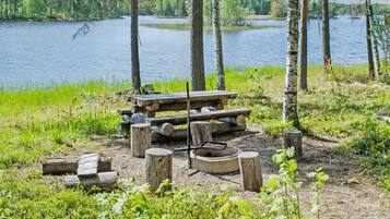 Un campamento junto al lago con una mesa de picnic de madera y un brasero rodeado de troncos.