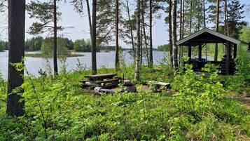 A lakeside cabin with a wooden deck, surrounded by dense forest and a clear view of the lake.