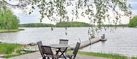 Eine Holzterrasse mit Tisch und Stühlen mit Blick auf einen ruhigen See, mit einem Steg, der ins Wasser führt.