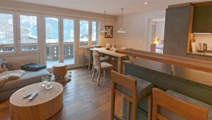 Una sala de estar moderna con un banco de madera, una mesa de centro redonda y una zona de comedor con una mesa larga y sillas.