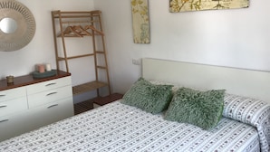 A bedroom with a bed, a dresser, a wooden ladder, and two wall-mounted paintings.