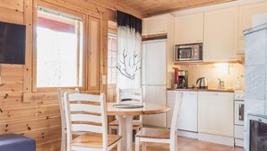 Ein Holzinterieur mit einem runden Esstisch, weißen Stühlen, einer Küchenzeile mit Mikrowelle, Herd und Kühlschrank.