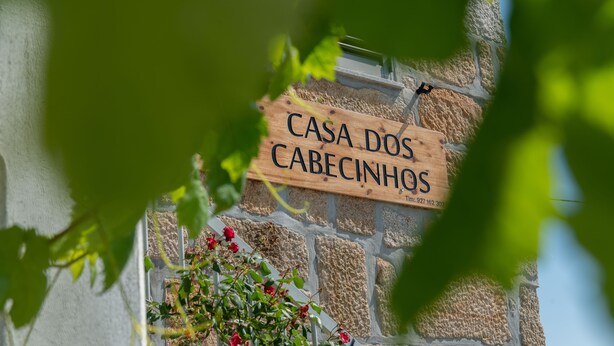 Un cartello in legno con la scritta "CASA DOS CABECINHOS" su un muro di pietra.