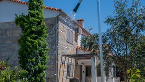 A stone building with a tiled roof, a wooden sign reading "BEM-VINDOS", and a metal water spout.