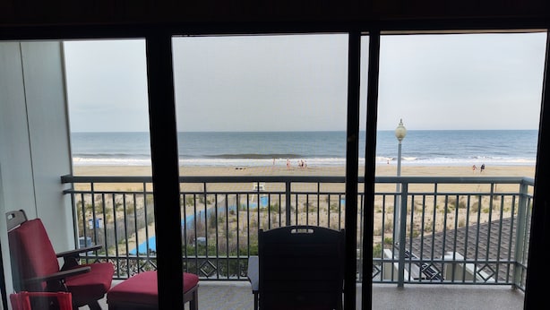 A balcony with a view of the beach, featuring a railing, a chair, and a table. - Edgewater House - Ocean Front Units With Spectacular Views! (Rehoboth Beach)