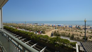 A beach view from a balcony with a clear sky, umbrellas, and people. - Edgewater House - Ocean Front Units With Spectacular Views! (Rehoboth Beach)