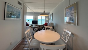 Un comedor con una mesa redonda y sillas blancas, un televisor al fondo y obras de arte en las paredes.