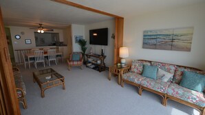 A living room with a sofa, coffee table, and chairs. There is a television mounted on the wall and a painting above it. - Edgewater House - Ocean Front Units With Spectacular Views! (Rehoboth Beach)