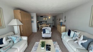 A living room with two sofas, a coffee table with a plant and remotes, a dining area with a table and chairs, and a kitchen in the background. - Edgewater House - Ocean Front Units With Spectacular Views! (Rehoboth Beach)