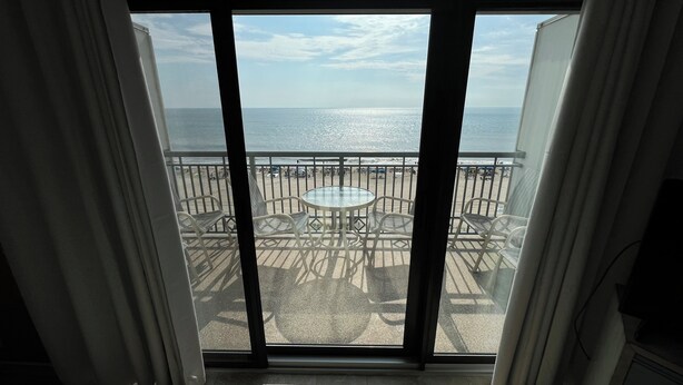 A balcony with a glass table and chairs, overlooking a beach with umbrellas and people. - Edgewater House - Ocean Front Units With Spectacular Views! (Rehoboth Beach)
