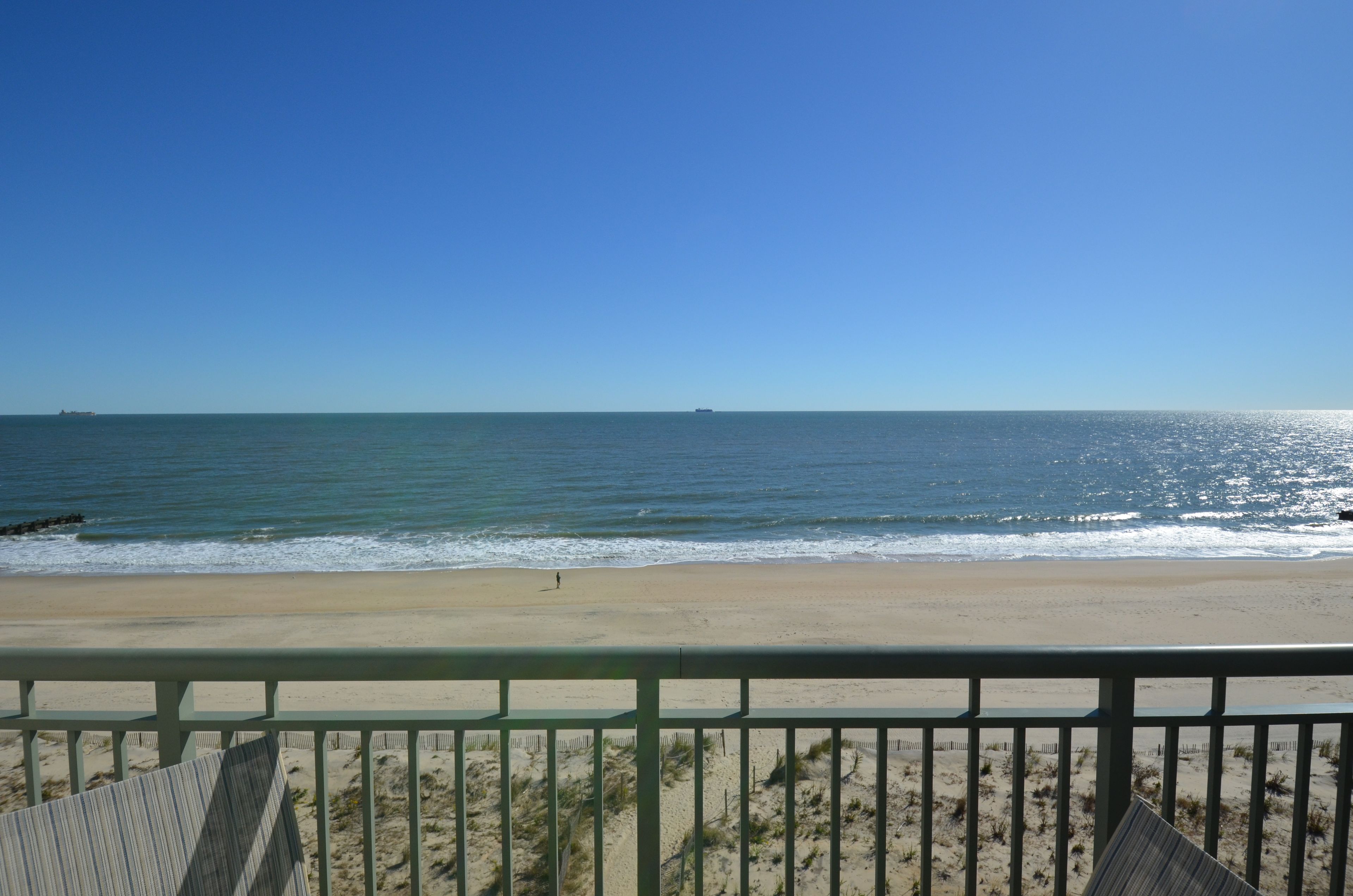 Une vue sur la plage, avec un ciel dégagé, une côte sablonneuse et un navire au loin.