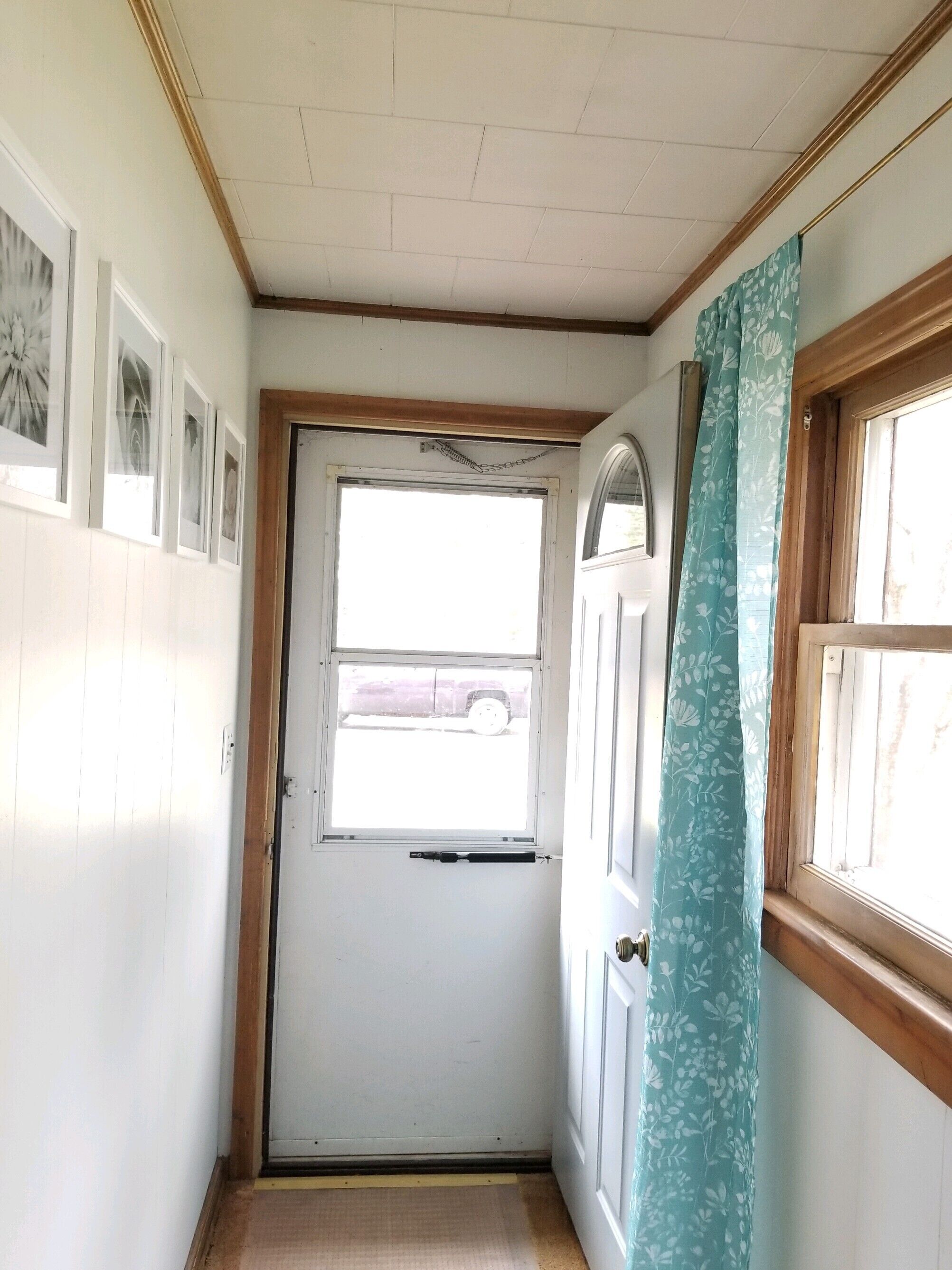 A narrow hallway with a white door, a window with a view of a vehicle outside, and a wall with framed pictures.