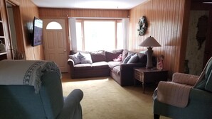A living room with a sofa, a chair, a lamp, and a television mounted on the wall. - Reggie's Northwoods Retreat (St Germain)