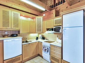 A compact kitchen with wooden cabinets, a microwave, a refrigerator, a dishwasher, and a stove.