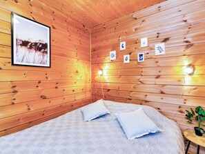 Een houten kamer met een bed, kussens, een ingelijst foto en wandlampen.