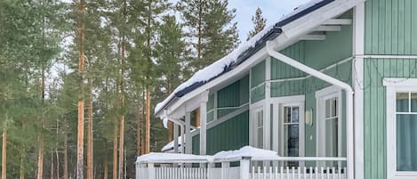 A green building with a white porch and snow accumulation.