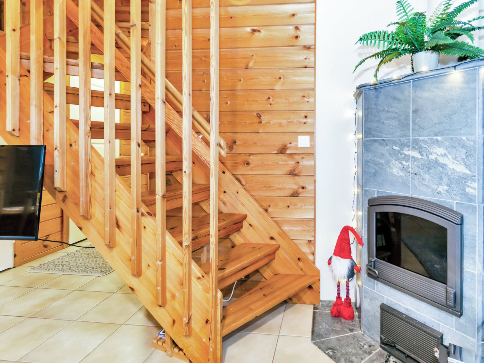 A wooden staircase leading to an upper level, a fireplace with a stone surround, and a potted fern on the mantel.