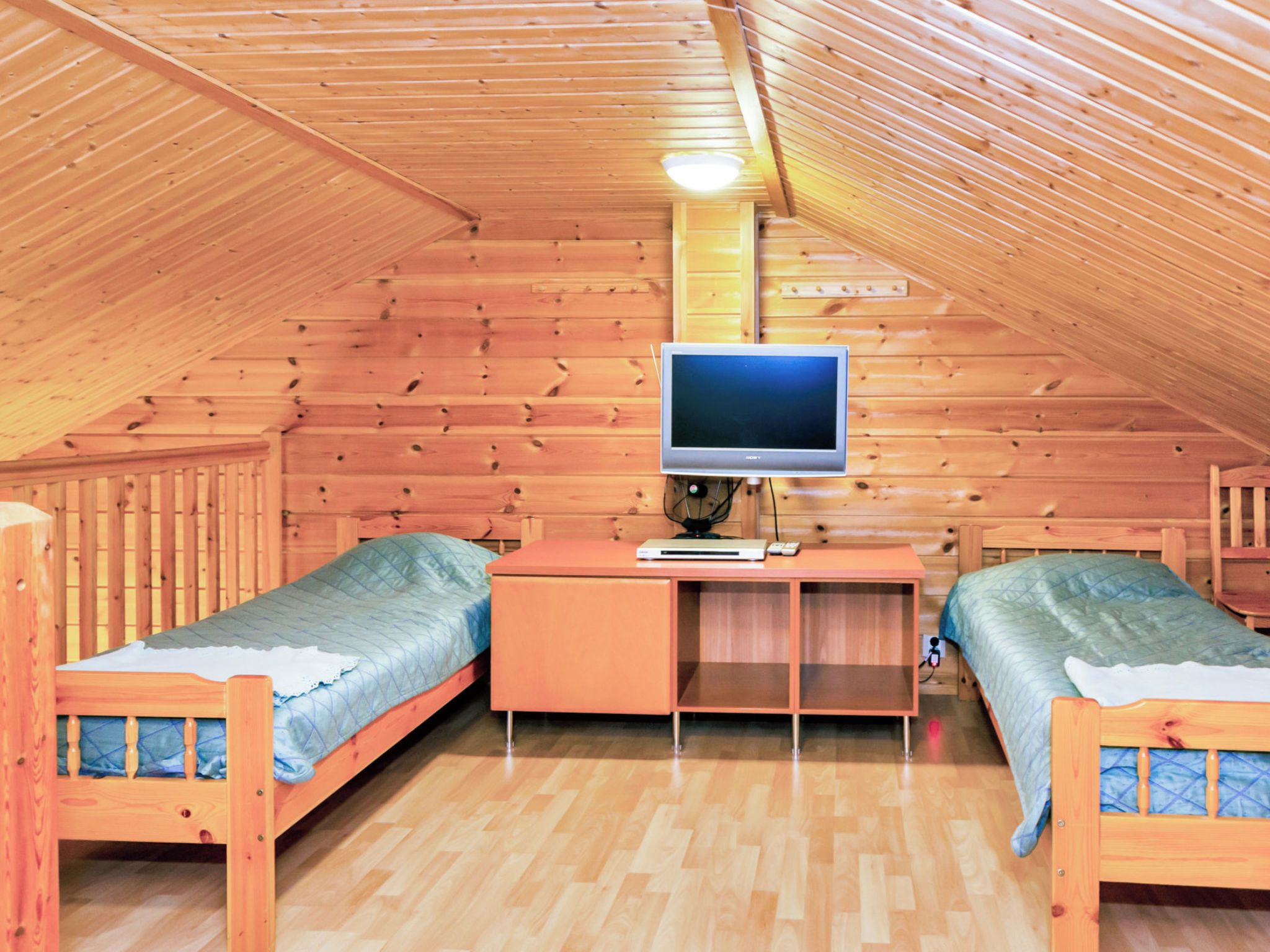 Un dormitorio acogedor en el ático con dos camas de madera, un escritorio con computadora y un televisor.