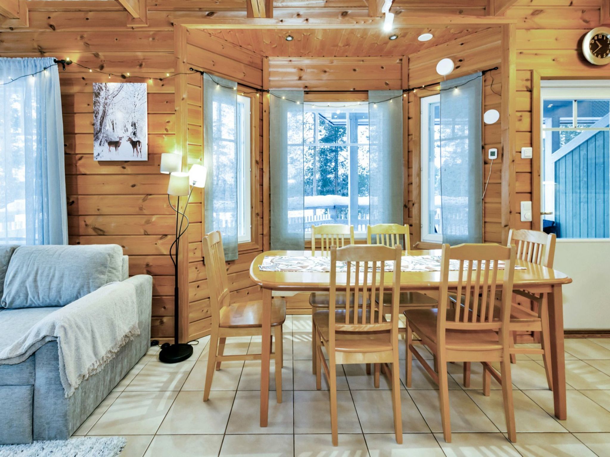 Interior acolhedor de uma cabana com uma mesa de jantar rodeada por cadeiras, um sofá e um abajur.