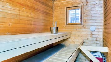 Un sauna avec des murs en bois, un banc, une fenêtre et un seau en métal.