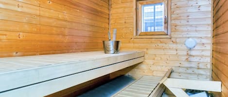 A sauna room with wooden walls, a bench, a window, and a metal bucket.