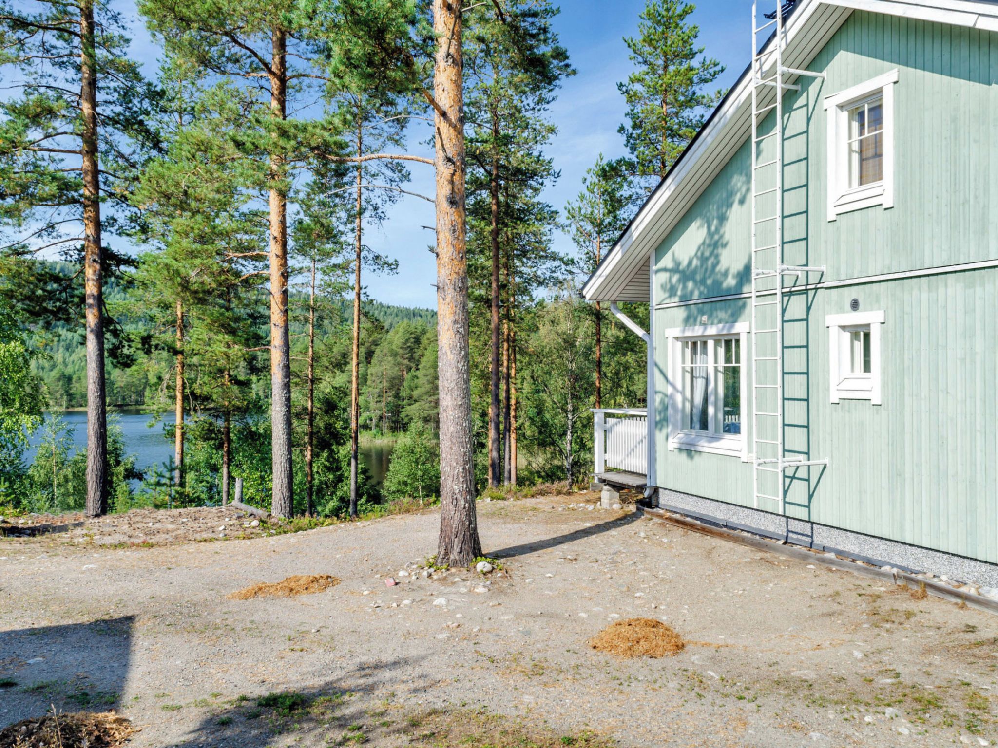 Ein Haus mit Kopfsteinpflasterauffahrt, einer Holzterrasse und Blick auf einen See, der von hohen Kiefern umgeben ist.