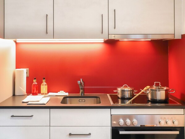 A modern kitchen with white cabinets, a red backsplash, stainless steel appliances, and a built-in oven. - Rossignol B by Interhome (Zermatt)