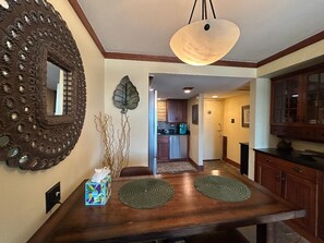 A dining area with a wooden table, two placemats, a decorative mirror, and a hanging light fixture.