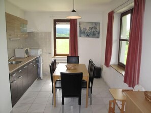 Eine kompakte Küche mit Essbereich, ausgestattet mit einem Tisch, Stühlen, einer Mikrowelle und einem Fenster mit Vorhängen.