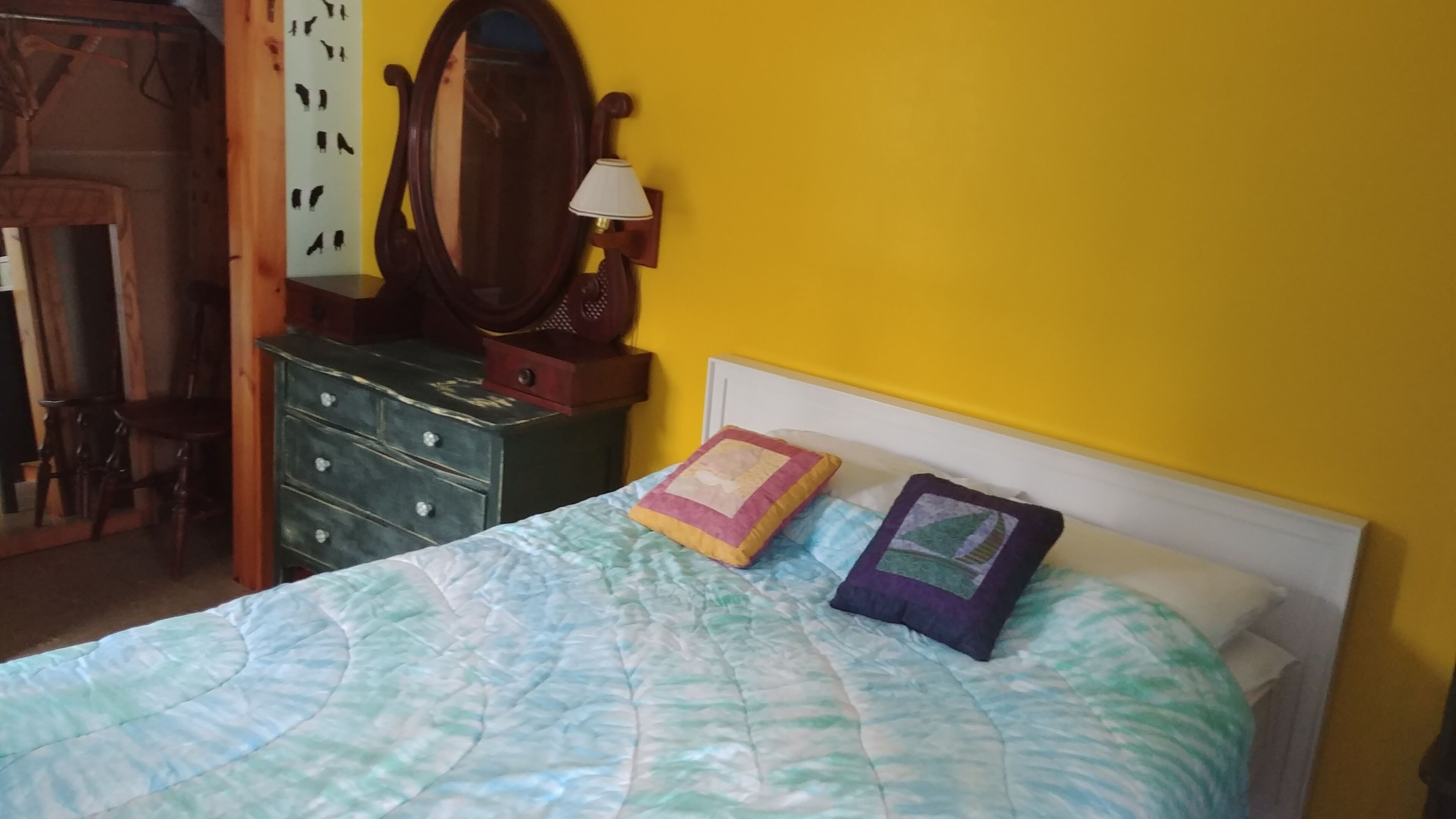 Een slaapkamer met een bed, een dressoir, een spiegel en een wandlamp.