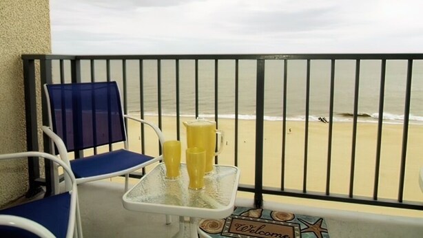 A balcony with a view of the beach, a welcome sign, and a table with drinks.