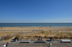 A beach view from a wooden deck with benches, a fence, and a clear sky. - OCEAN FRONT CONDO.  ENJOY YOUR MORNING COFFEE SITTING ON YOUR PRIVATE BALCONY WATCHING THE SUNRISE. (Rehoboth Beach)
