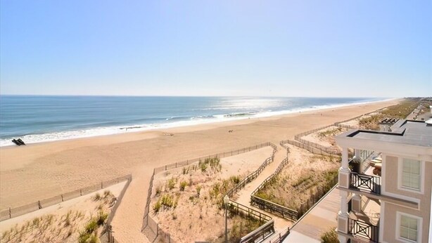 Vista de una playa con un paseo marítimo de madera que lleva al océano, una playa de arena y un edificio con balcones.