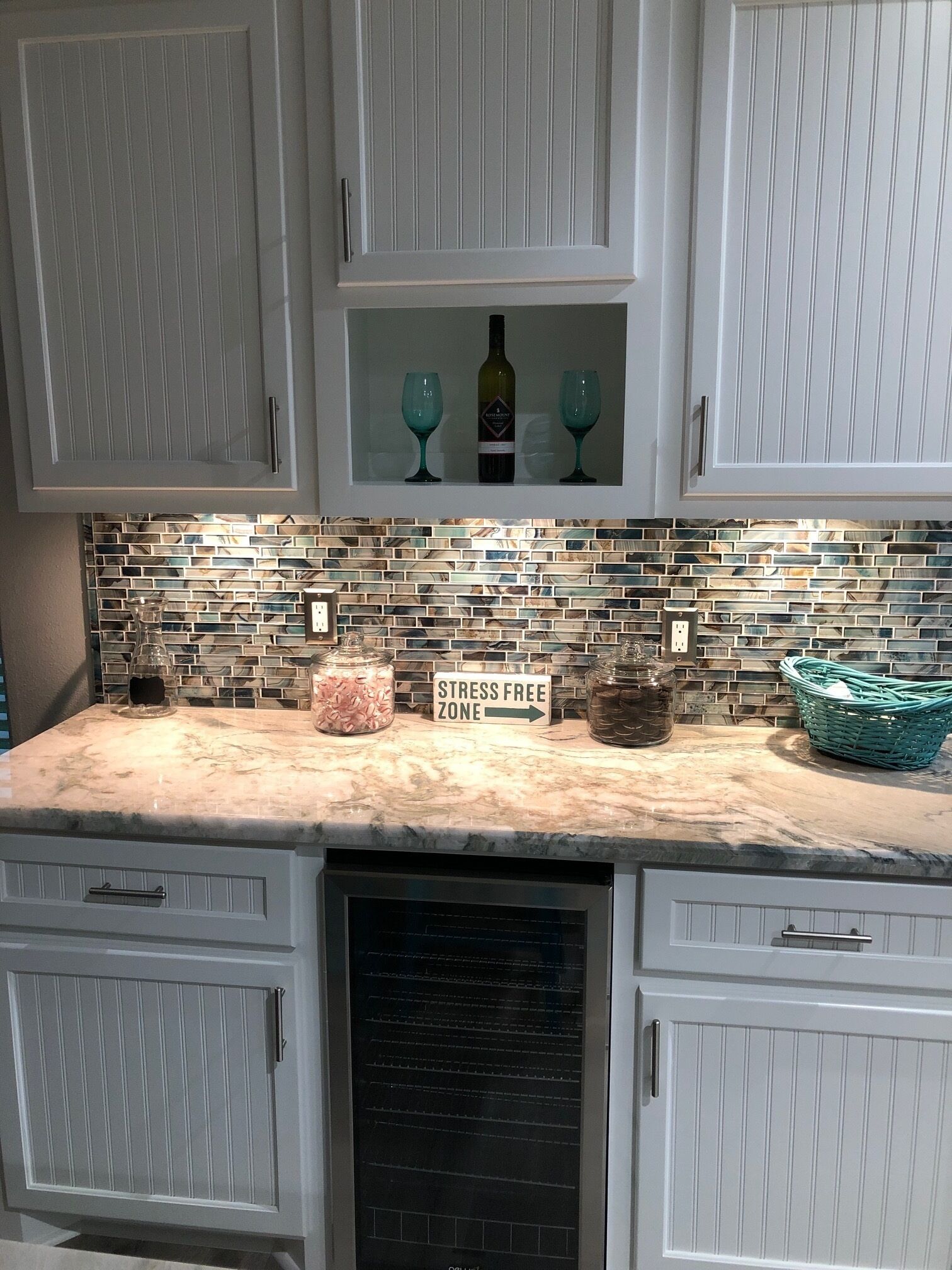 A kitchen with white cabinets, a marble countertop, a glass backsplash, and a sign indicating a stress-free zone.